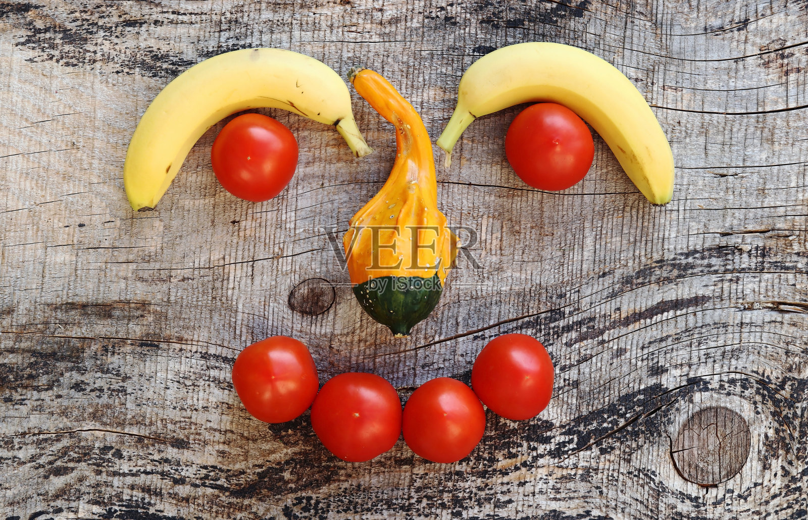 一张由香蕉、西红柿和南瓜组成的脸，木制背景照片摄影图片