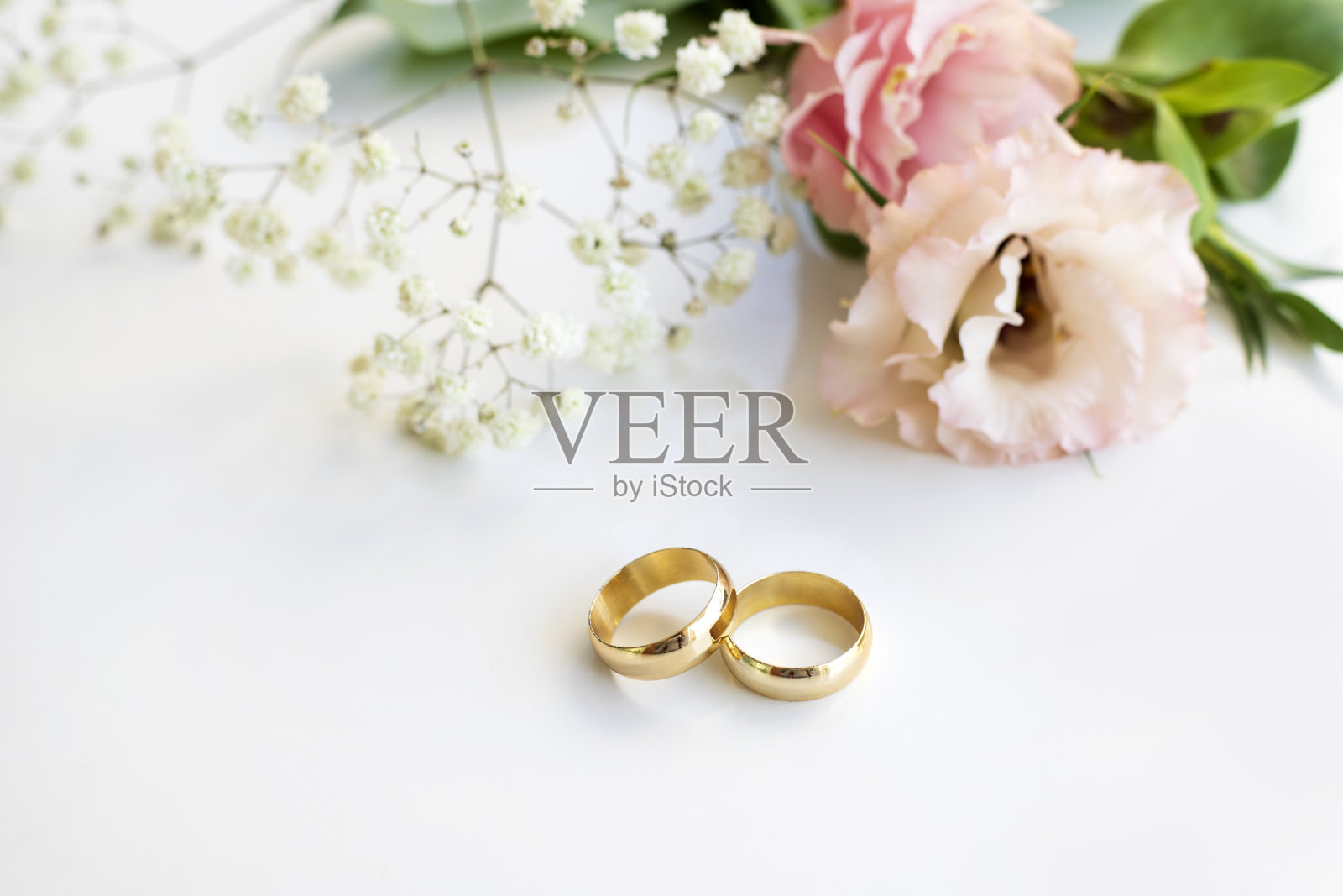 白色背景上有粉红色的花和两枚金色的结婚戒指。照片摄影图片