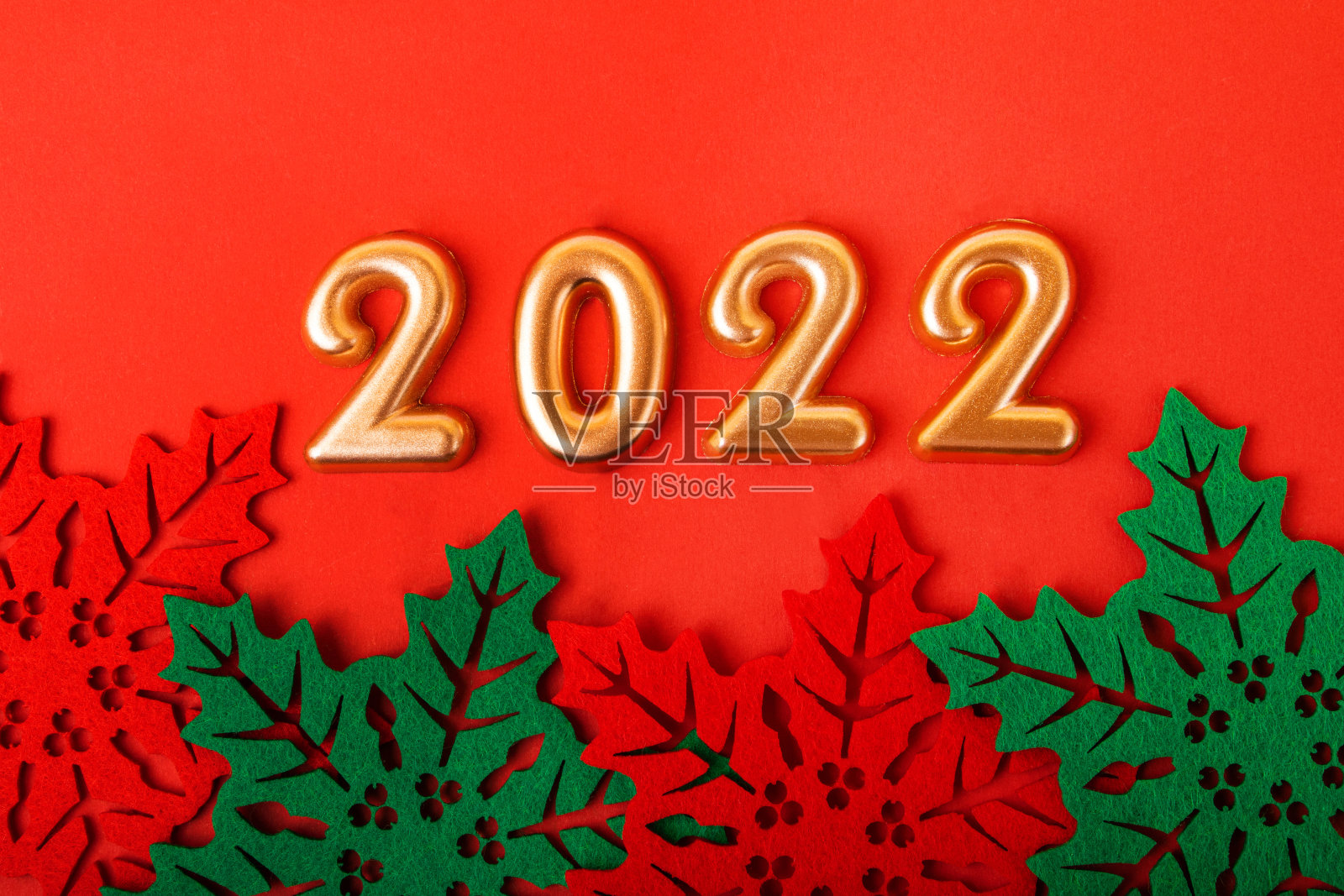 红色背景上的金色数字是2022。下面是美丽的冬青树叶子。新年的背景。照片摄影图片
