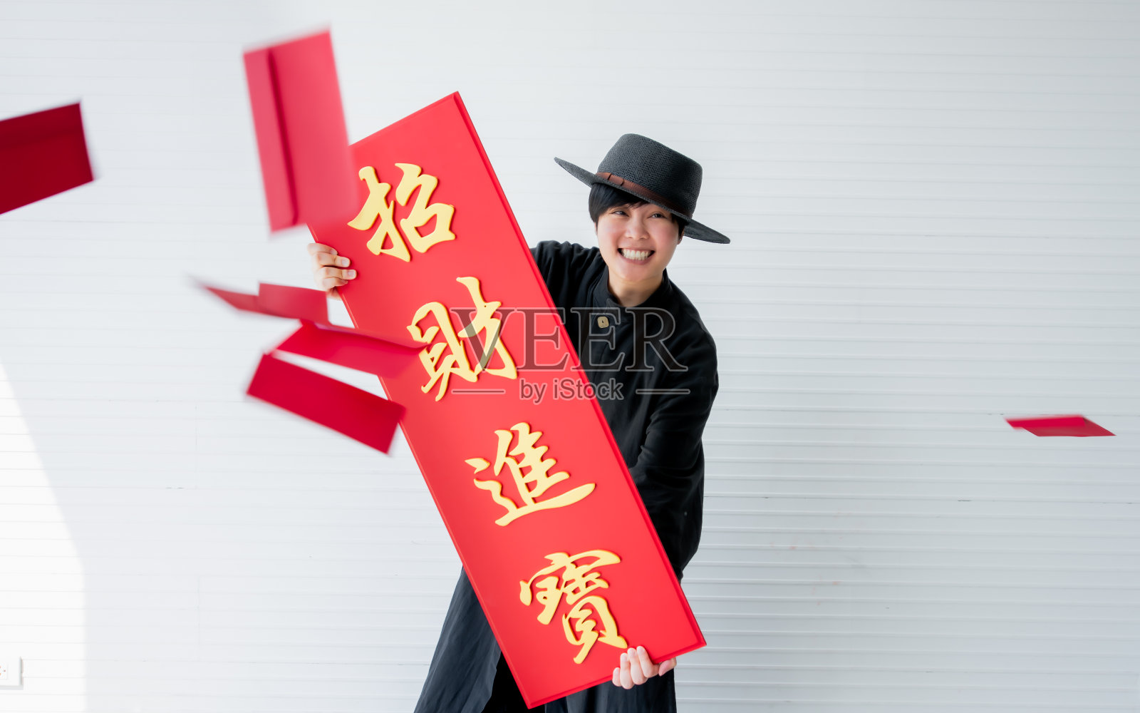 亚洲妇女身穿黑色中国传统服饰，头戴礼帽，手持象征财富、富裕、富有的标志，空气中飘荡着红包。庆祝中国新年概念。照片摄影图片