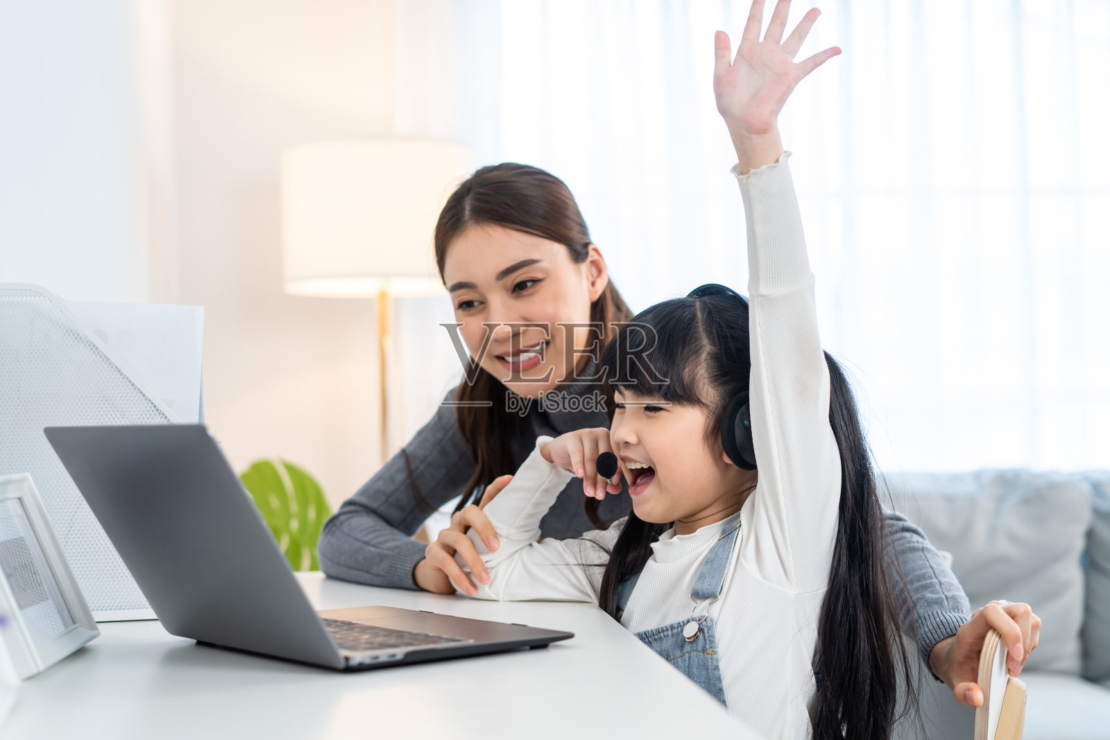 亚洲小女孩孩子学习在线课程在家里与母亲。学龄前儿童使用笔记本电脑做作业，由学校老师通过数字远程互联网在妈妈的支持下在家上学。照片摄影图片
