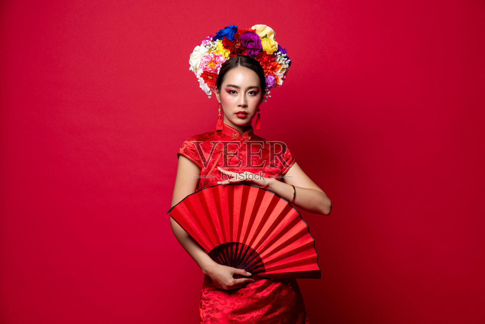 美丽优雅的亚洲妇女穿着传统服装与花冠持有红色扇子在孤立的工作室背景为中国新年的概念照片摄影图片