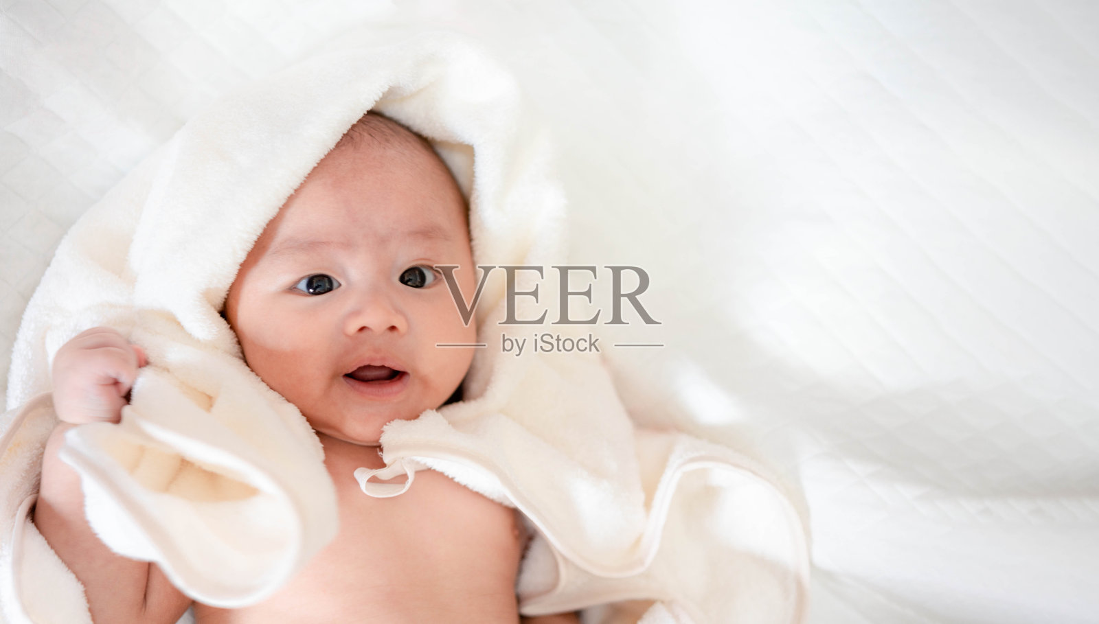 床上可爱的亚洲新生儿。小男孩看着镜头，露出开心的笑容。天真的小婴儿，刚出生的第一天。母亲一天的概念。照片摄影图片