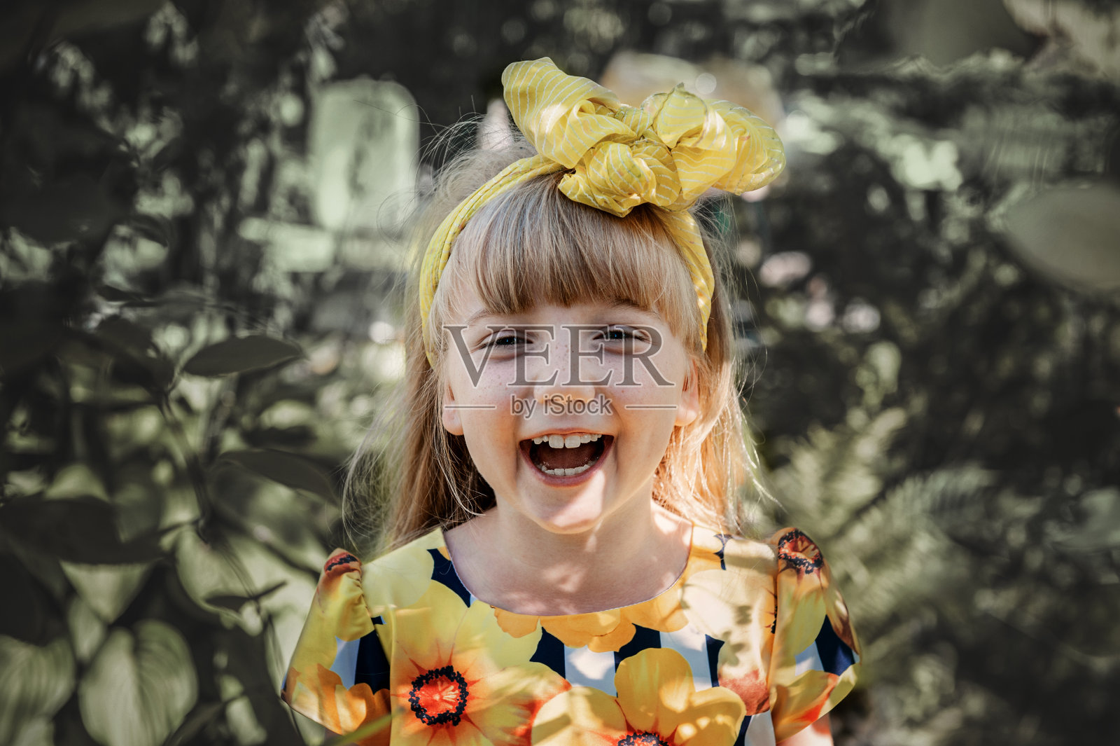 在公园里，一个微笑的漂亮的蓝眼睛的女孩，淡红色的头发，戴着黄色的蝴蝶结。童年，大自然，夏日的概念。前面的观点，一个可爱的婴儿与黄色美丽的弓照片摄影图片