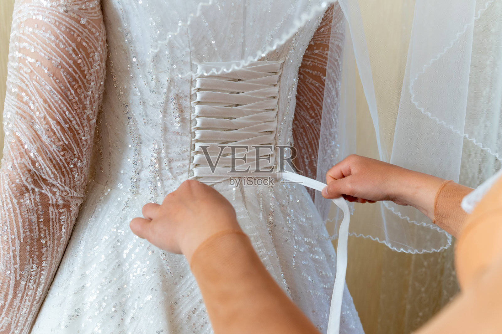 新娘帮忙穿婚纱。用带子束紧照片摄影图片