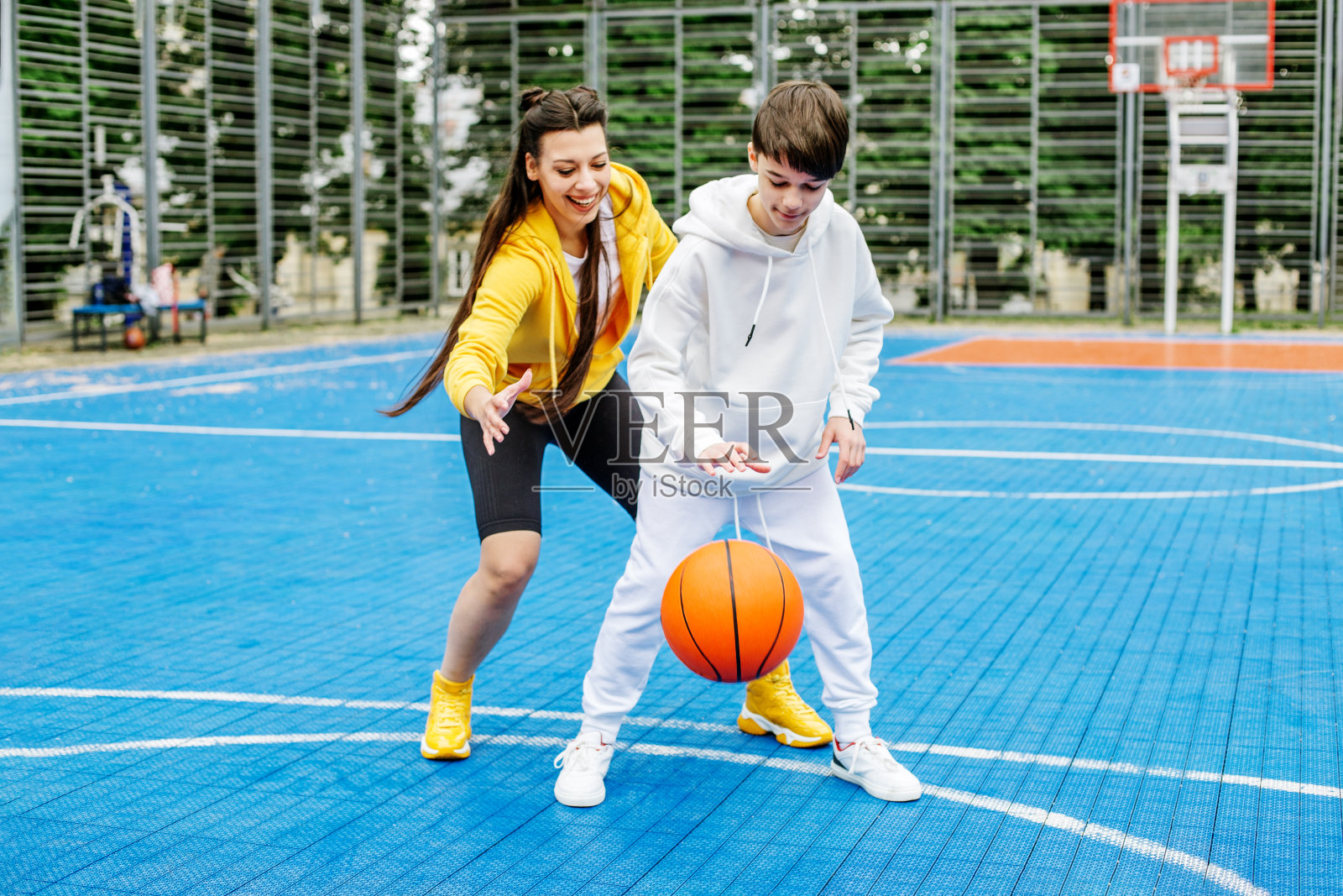 女孩和她十几岁的弟弟在露天的现代篮球场上打篮球。照片摄影图片_ID:426526476-Veer图库
