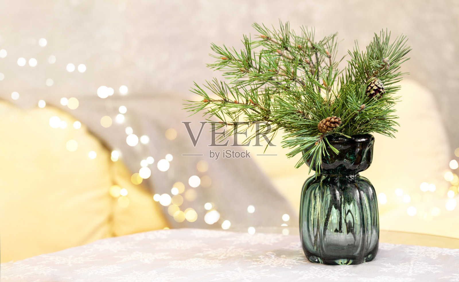 玻璃花瓶冷杉枝桌上，桌布客厅沙发和圣诞彩灯。照片摄影图片
