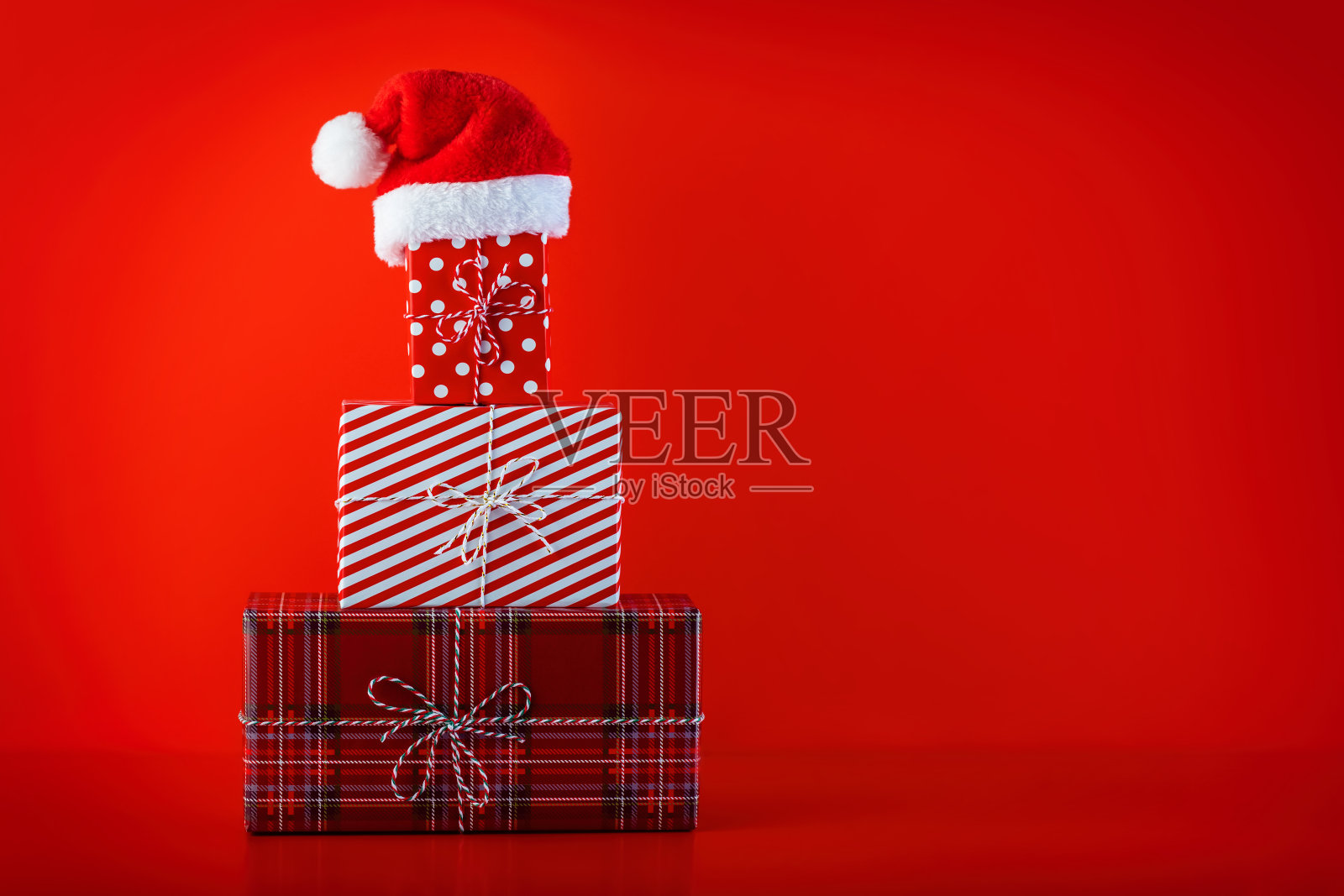 圣诞红色背景与圣诞礼物形状的圣诞树和圣诞老人帽子在顶部。照片摄影图片