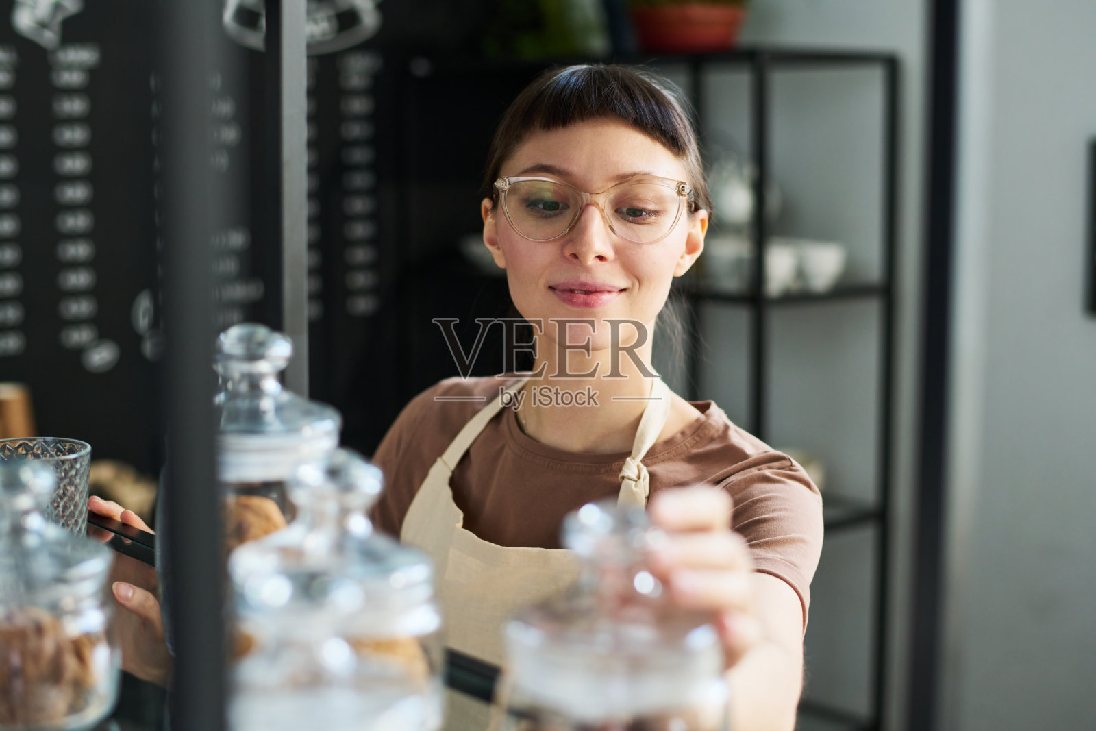 年轻微笑的女店员在检查装在小罐子里的花草茶照片摄影图片