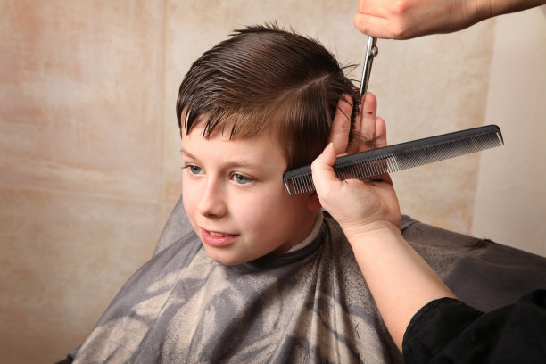 微笑的孩子在发型师理发师的手给小男孩做发型,特写男孩的时尚发型