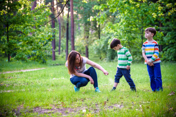 年轻女子母亲在森林徒步旅行前给她的两个儿子涂驱虫剂美丽的夏日白天
