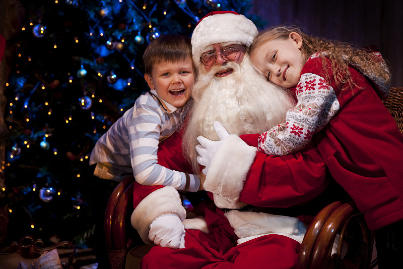 坐在椅子上的两个孩子拥抱着圣诞老人图片下载